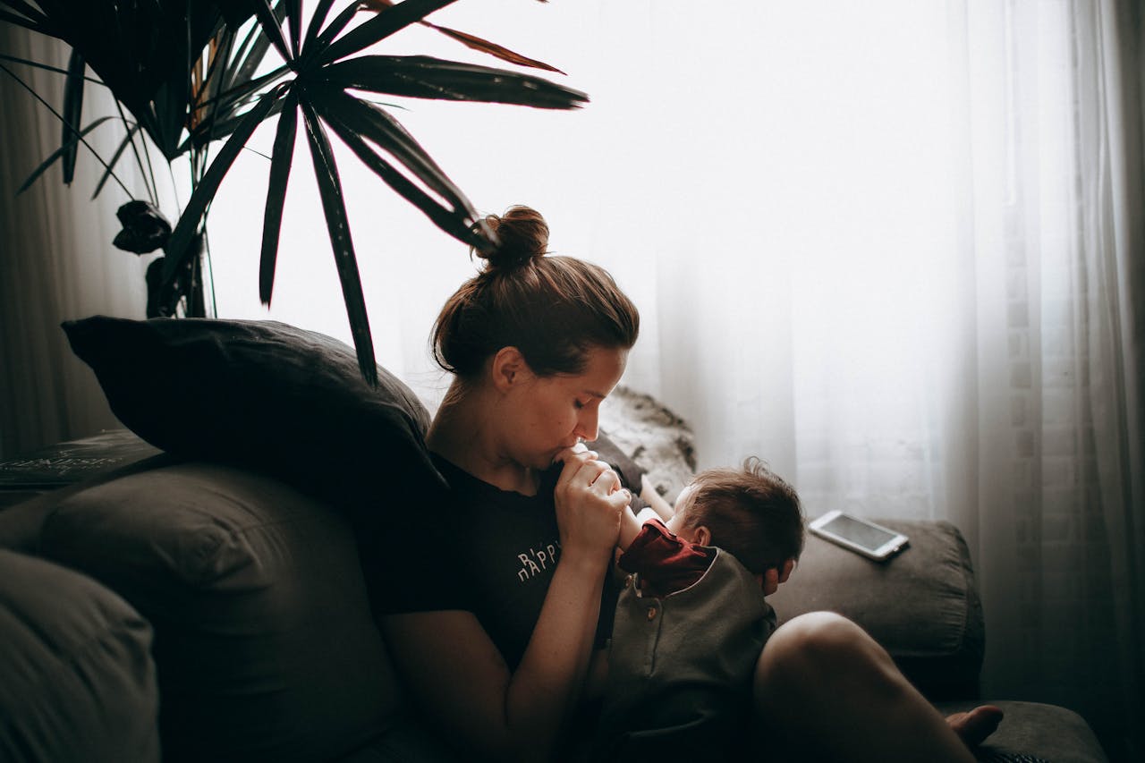 Une mère assise, portant un sweat rose, tient son bébé dans les bras et l’allaite dans une pièce au fond neutre.