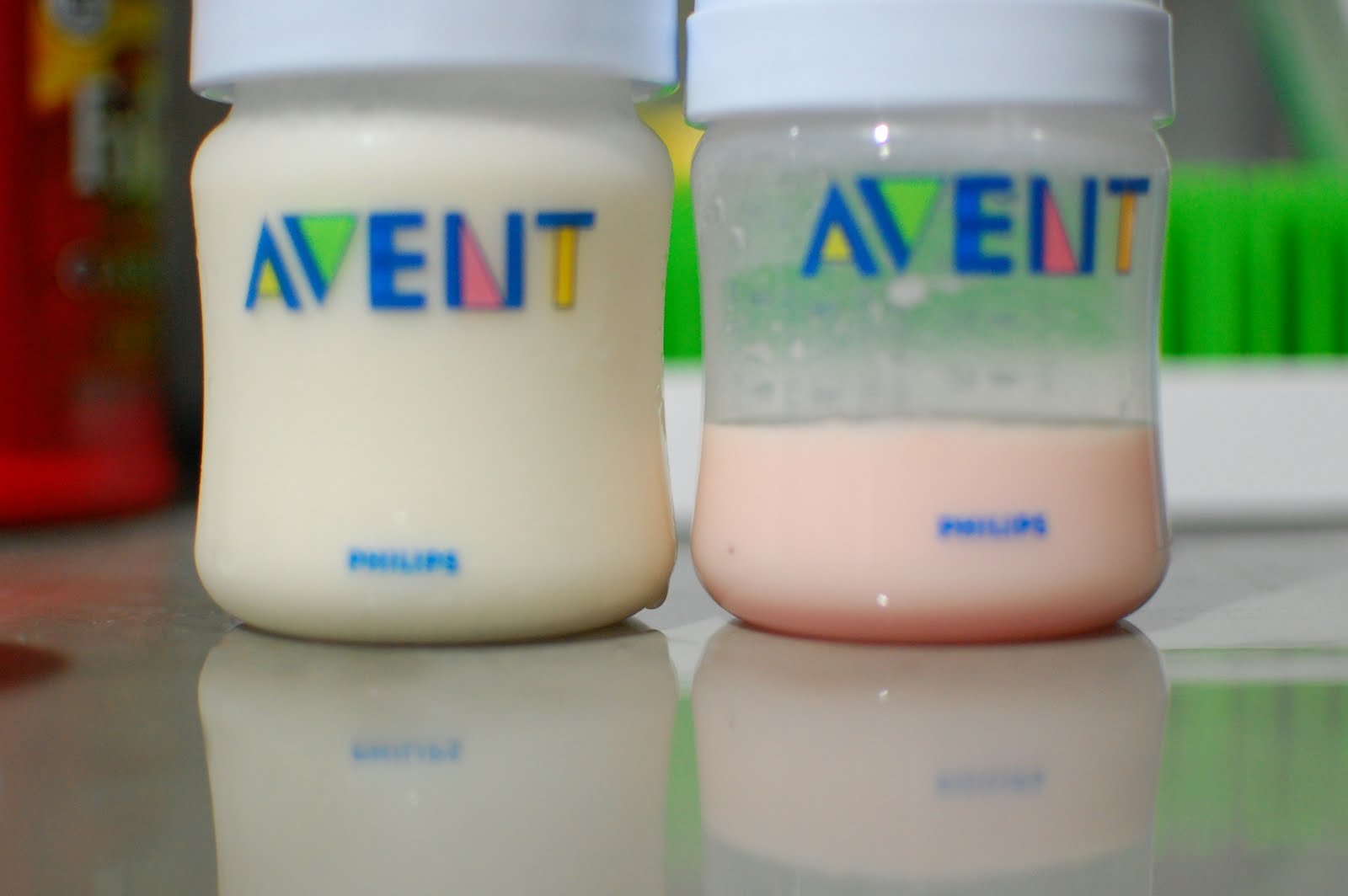 Gros plan sur deux petits biberons Philips Avent posés sur une surface réfléchissante, l’un rempli de lait maternel blanc et l’autre contenant du lait maternel légèrement rosé.