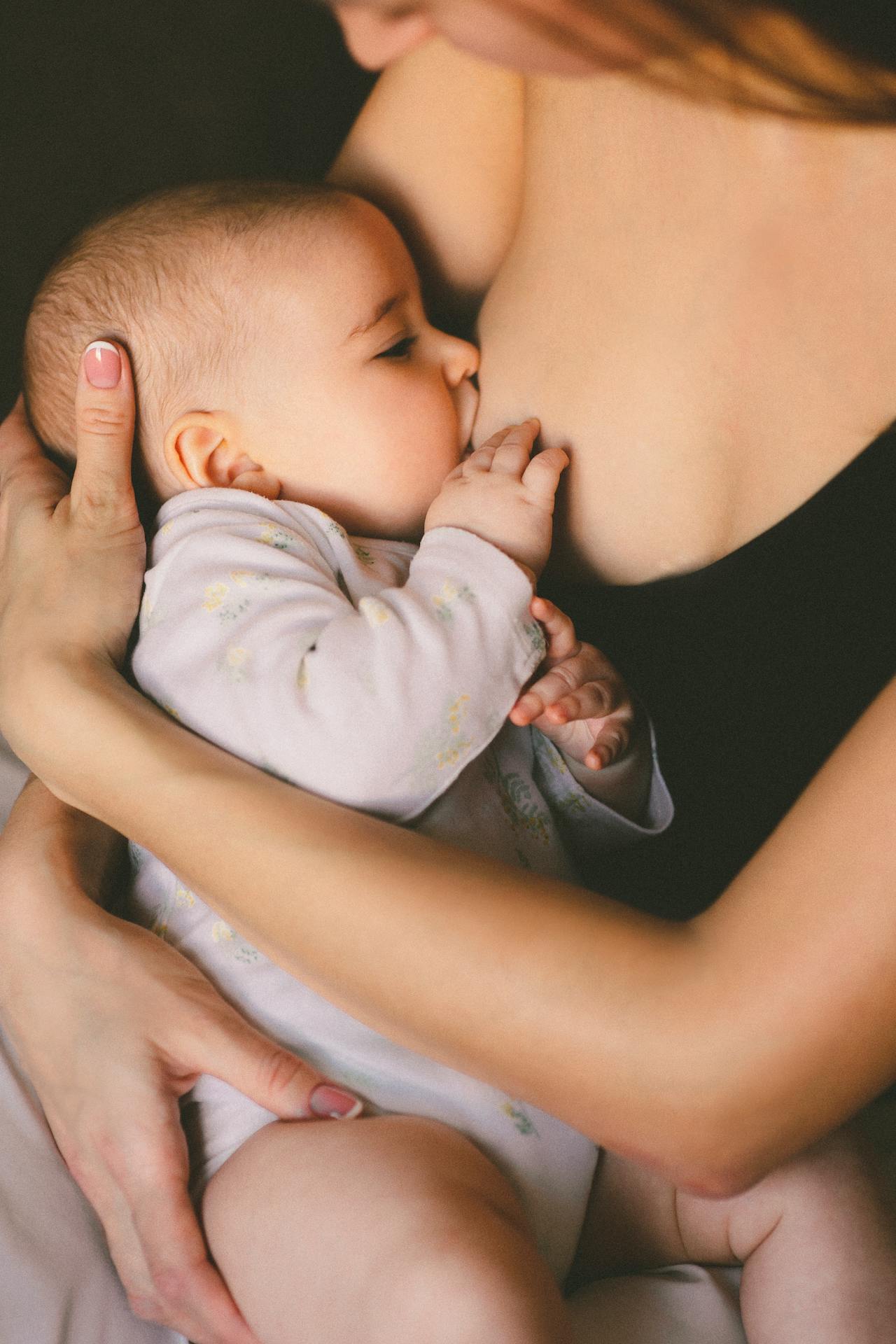Gros plan d’une mère tenant son bébé dans ses bras pendant qu’elle l’allaite au sein, dans une lumière douce et chaleureuse.
